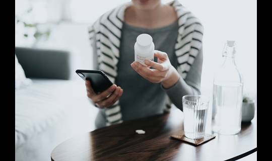 Woman looks at pill bottle and her phone